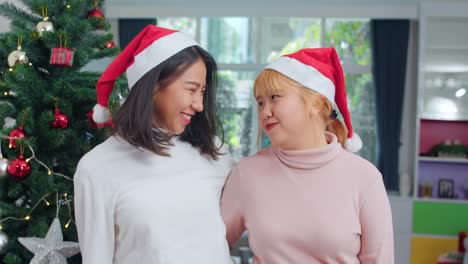 Asian-Lesbian-couple-celebrate-Christmas-festival.-LGBTQ-female-teen-wear-Christmas-hat-relax-happy-smiling-looking-at-camera-enjoy-xmas-winter-holidays-together-in-living-room-at-home.