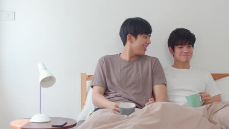 Asian-Gay-men-couple-talking-having-a-great-time-at-modern-home.-Young-Asia-lover-male-happy-relax-rest-drink-coffee-after-wake-up-while-lying-on-bed-in-bedroom-at-house-in-the-morning-concept.