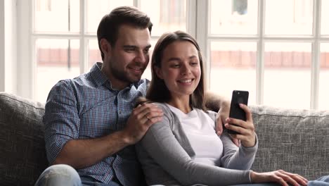 Happy-young-couple-using-smartphone-social-media-apps-at-home