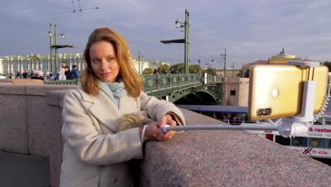 junge-Stadtfrau-macht-Foto-mit-Smartphone-und-Selfie-Stick,-im-Freien-auf-Brücke-in-der-Stadt