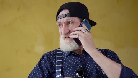 Front-view-of-happy-smiling-modern-bearded-senior-man-in-cap-which-having-phone-conversation-with-friend