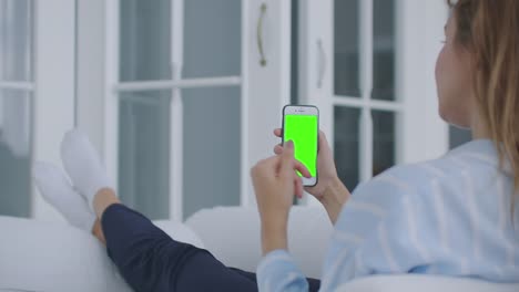 Woman-using-for-video-call-mobile-phone-vertical-green-screen.-Female-holding-in-hand-portable-gadget-close-up-indoors-home-living-room.-Mock-up-for-tracking-or-watching-content.