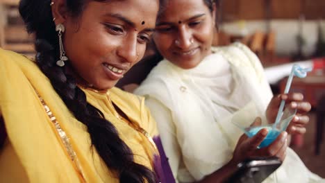 Two-women-chilling-sipping-drinks-using-technology-in-cafe