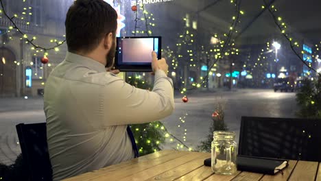 Businessman-takes-photo-by-tablet-app,-at-night,-in-cafe,-christmas