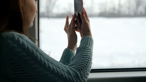 Young-girl-traveling-in-a-train-and-using-mobile-phone-to-take-a-photo-of-the-landscape-outside-the-window.-Beautiful-woman-takes-pictures-on-a-smartphone.-Close-up