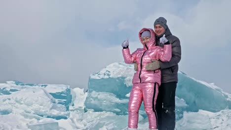 Young-couple-has-fun-during-winter-walk-against-background-of-ice-of-frozen-lake.-Lovers-are-having-fun,-laughing,-jumping,-kissing-near-a-huge-blue-ice-floe.-Honeymoon.-Love-story.