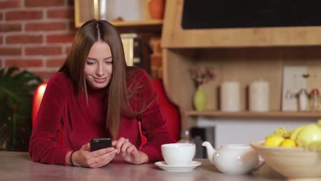 Mujer-joven-navegando-por-internet,-revisar-novedades-en-redes-sociales-durante-el-uso-de-smartphone-en-la-cocina.