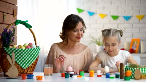 Mom-teaching-daughter-how-to-color-Easter-eggs,-family-preparing-for-holiday