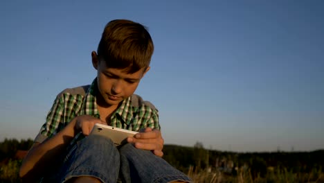 boy-use-tablet-sitting-in-field-at-sunset,-outdoors