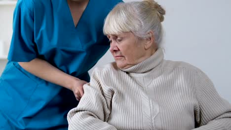 Medical-worker-moving-aside-sad-disabled-aged-female-in-wheelchair,-loneliness