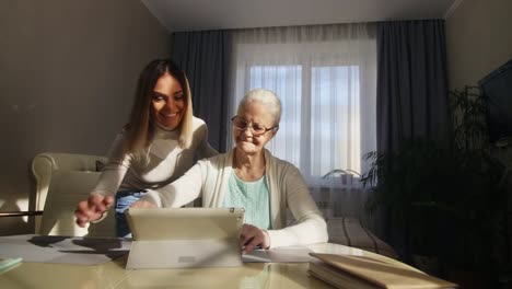 Senior-mujer-que-aprende-la-tableta-con-la-ayuda-de-la-nieta-adulta