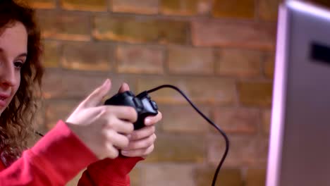 Close-up-portrait-of-concentrated-young-female-blogger-actively-playing-video-game-using-joystick-on-bricken-wall-background.