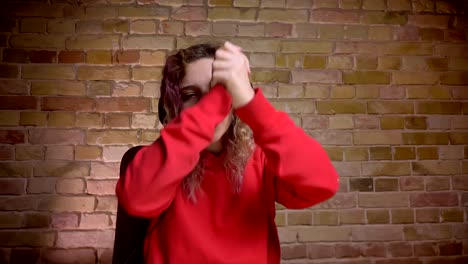 Close-up-portrait-of-blogger-in-headphones-in-front-of-camera-and-happily-putting-hands-together-on-bricken-wall-background.