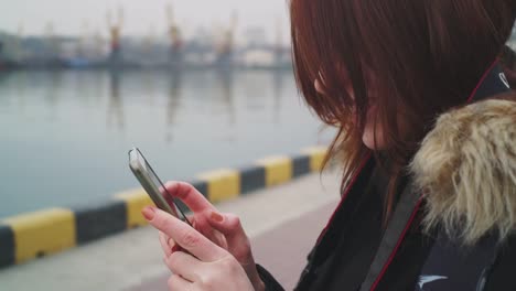 Close-up-shot-of-beautiful-woman-using-smart-phone-technology-app-walking-on-the-street-in-a-warm-jacket-with-a-fluffy-hood