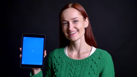 Closeup-portrait-of-attractive-caucasian-female-showing-the-screen-on-the-tablet-and-making-thump-up-looking-at-camera-and-smiling