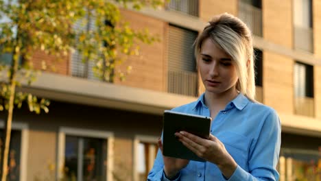 Portrait-of-young-girl-using-tablet-computer-in-the-park.-Modern-architecture-building-background