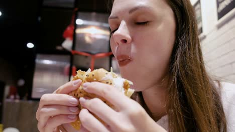 Woman-eating-a-hamburger-with-relish-and-delight-in-cafe.