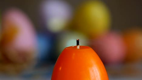 Candles-made-in-shape-of-easter-egg.-Burning-candles.-Green-and-orange-candles-.-Sliding,-close-up.-Orange-candles-extinguished-from-the-air.