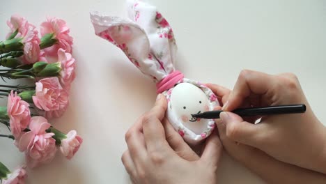 Women's-and-children's-hands-hold-chicken-egg-decorated-for-Easter-bunny-in-hands,-paint-rabbit's-face-with-marker.