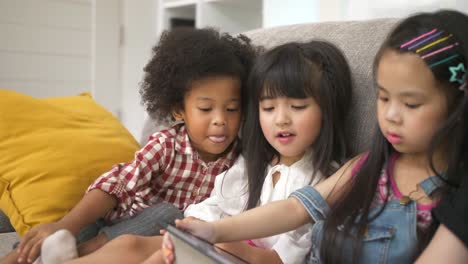 Gruppe-von-Kindern,-die-mit-digitalem-Tablet-zusammen-auf-dem-Sofa-zu-Hause-spielen,-und-lächelnd,-Kinder-auf-digitalem-Tablet-im-Wohnzimmer.