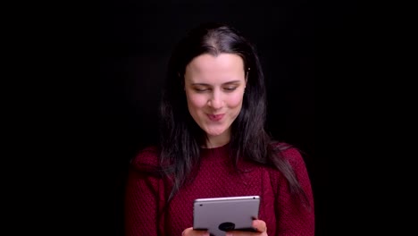 Closeup-portrait-of-young-caucasian-female-with-black-hair-color-using-the-tablet-and-laughing-with-background-isolated-on-black