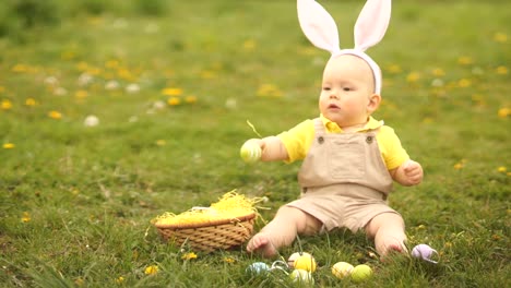 Lovely-baby-in-an-Easter-bunny-costume-collects-Easter-eggs-in-a-basket-sitting-on-the-grass-in-the-park.-Spring-picnic,-happy-easter-family