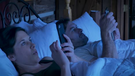 Man-and-woman-lying-in-bed-looking-at-their-mobile-phones-at-night