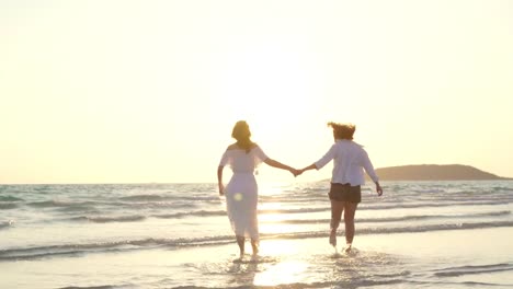 Junges-asiatisches-lesbisches-Paar-läuft-am-Strand.-Schöne-Freundinnen-freuen-sich,-sich-bei-Sonnenuntergang-am-Abend-am-Strand-am-Meer-zu-vergnügen.-Lifestyle-lesbisches-Ehepaar-reist-nach-Strandkonzept