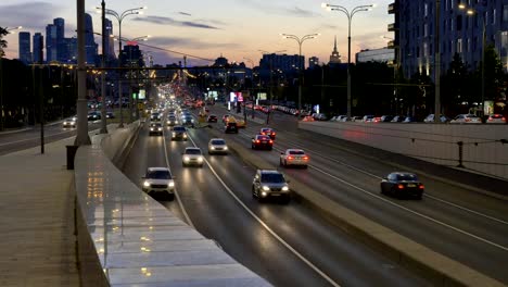 cars-drive-along-wide-evening-city-street-past-buildings