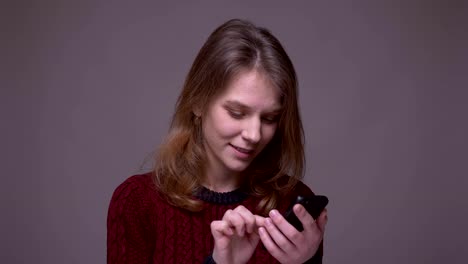 Joven-estudiante-que-trabaja-con-teléfono-inteligente-se-convierte-en-cámara-y-sonríe-sobre-fondo-gris.