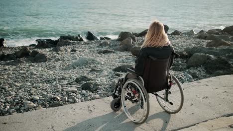 Una-mujer-discapacitada-está-sentada-en-silla-de-ruedas-cerca-de-la-orilla-del-mar-y-observando-olas