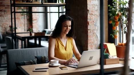 Attractive-girl-using-laptop-in-cafe-typing-smiling-working-in-cafe-alone