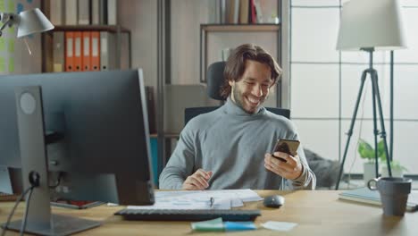 Guapo-emprendedor-de-pelo-largo-sentado-en-su-escritorio-en-la-oficina-trabaja-en-computadora-de-escritorio,-trabajar-con-documentos,-corregir-gráficos,-dibujar-gráficos