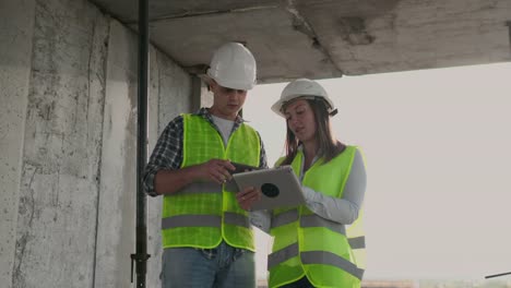 Ingenieros-diseñadores-se-paran-en-el-techo-del-edificio-en-construcción-y-discutir-el-plan-y-el-progreso-de-la-construcción-utilizando-una-tableta-y-un-teléfono-móvil