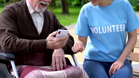 Mujer-voluntaria-enseñando-a-un-anciano-discapacitado-en-silla-de-ruedas-cómo-usar-el-teléfono-celular