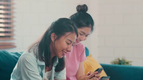 Young-Asian-Lesbian-women-couple-using-mobile-phone-check-social-media-on-internet-together-while-lying-sofa-in-living-room.