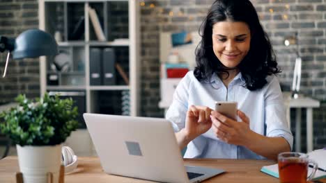 Beautiful-young-woman-texting-with-smartphone-touching-gadget-screen-at-work