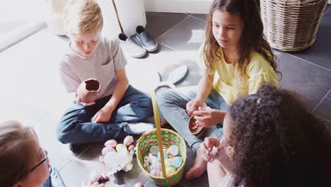 Overhead-view-of-group-of-children-sitting-on-floor-indoors-opening-and-eating-chocolate-Easter-eggs---shot-in-slow-motion