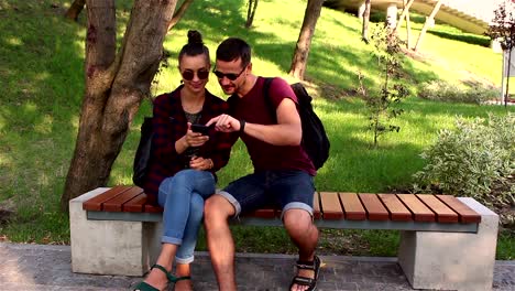 Young-loving-couple,-on-a-sunny-day,-is-actively-discussing-a-new-smartphone-while-sitting-on-a-bench-in-the-park.