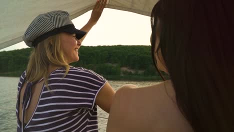 zwei-fröhliche-junge-Frauen-entspannen-auf-Segelboot-schwimmen-auf-Fluss-bei-Sonnenuntergang