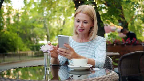 Cámara-lenta-de-la-mujer-feliz-usando-la-pantalla-táctil-del-teléfono-inteligente-en-el-café-exterior