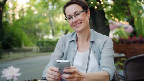 Lächelnde-Dame-mit-Smartphone-berühren-Bildschirm-lächelnd-in-Straßencafé-draußen