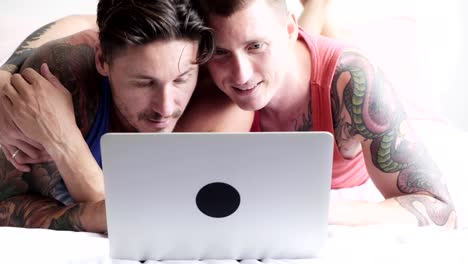 Gay-couple-in-bed-using-laptop-computer.-Hugging.