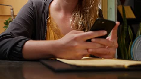 Happy-girl-uses-a-smartphone,-writes-a-message,-chatting.-Young-woman-looking-for-information-in-the-phone.-Sitting-in-restaurant-with-friends.-Breakfast-time