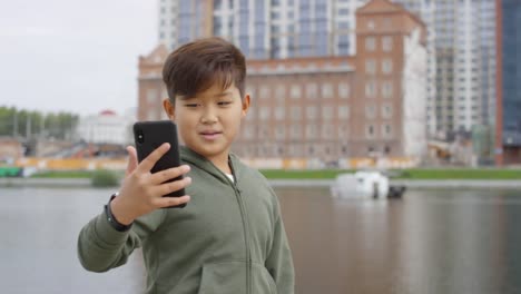 Asian-Boy-Walking-Outdoors-und-Talking-via-Video-Call-auf-dem-Smartphone