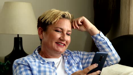 Woman-sitting-on-sofa-and-using-smart-phone-at-home