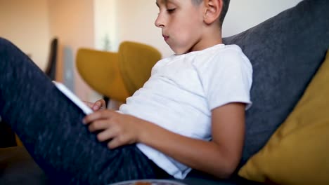 Young-boy-is-playing-games-on-tablet-and-eating-doughnut