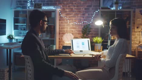 Compañeros-felices-desarrolladores-de-aplicaciones-de-teléfonos-inteligentes-discutiendo-el-trabajo-en-oficina-oscura