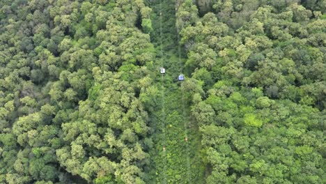 Cabina-del-teleférico-moviéndose-en-la-montaña-sobre-el-fondo-del-bosque-verde.-Teleférico-que-se-mueve-a-la-vista-aérea-de-montaña-verde-pico.-Teleférico-en-verano-resort