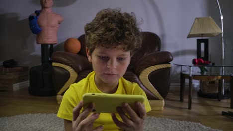 Cara-de-niño-caucásico-enfocado-viendo-dibujos-animados-o-películas-en-la-pantalla-del-teléfono-inteligente.-Niño-con-el-pelo-rizado-absorbido-por-Internet.-Redes-sociales,-tecnologías-modernas.-Cinema-4k-ProRes-HQ.